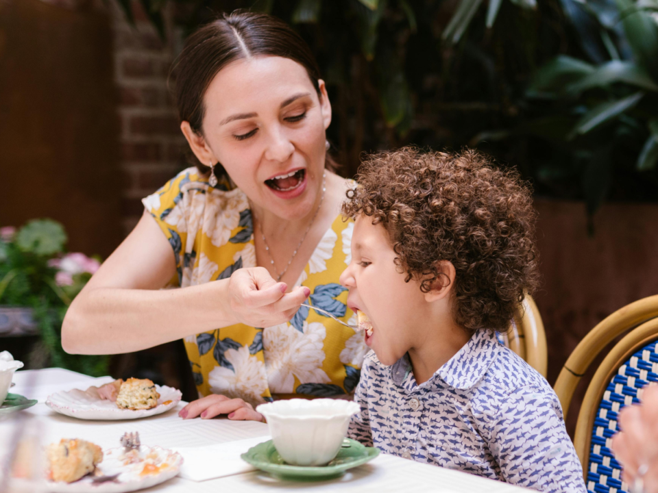 Mom is feeding the child at a table outside.