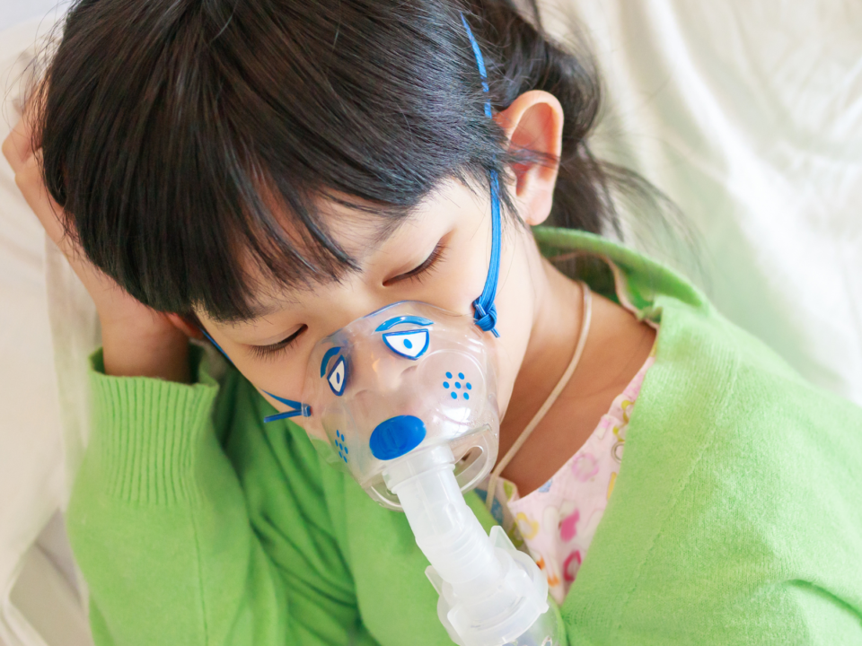 Child in lime green sweater with an nebulizer mask on while lying dow with eyes closed.