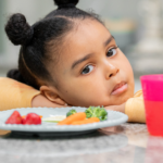 Child sitting at the dinner table and won't eat the food in front of her.