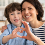 Mom and son sitting on a couch and connecting a heart sign with their fingers.