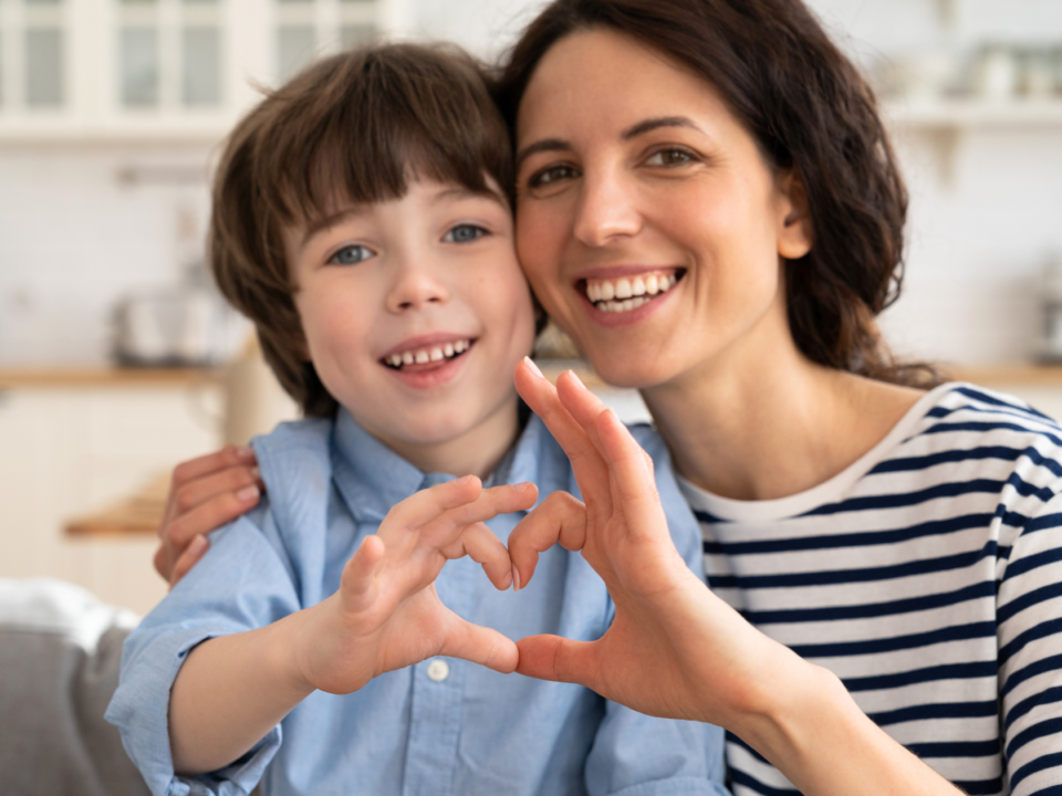 Mom and son sitting on a couch and connecting a heart sign with their fingers.