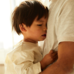 A young child is not feeling well and is being held by his dad.